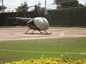 Un helicóptero estacionado sobre una superficie de hormigón con un césped y un seto al fondo.