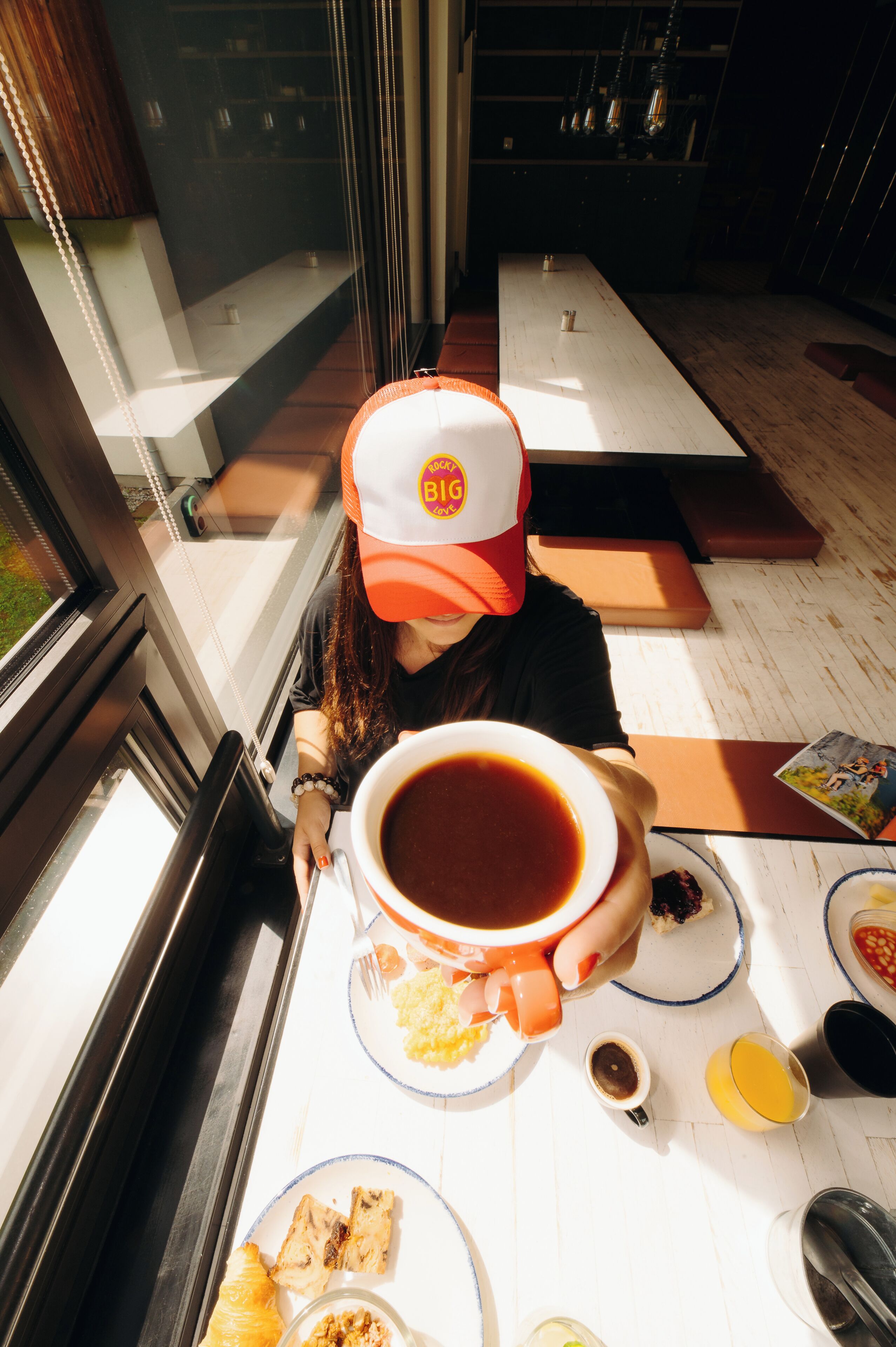 Une personne assise à une table, devant une tasse de café, une assiette de nourriture et un menu.