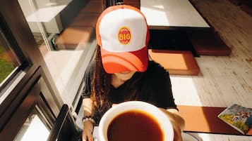 Une personne assise à une table, devant une tasse de café, une assiette de nourriture et un menu.