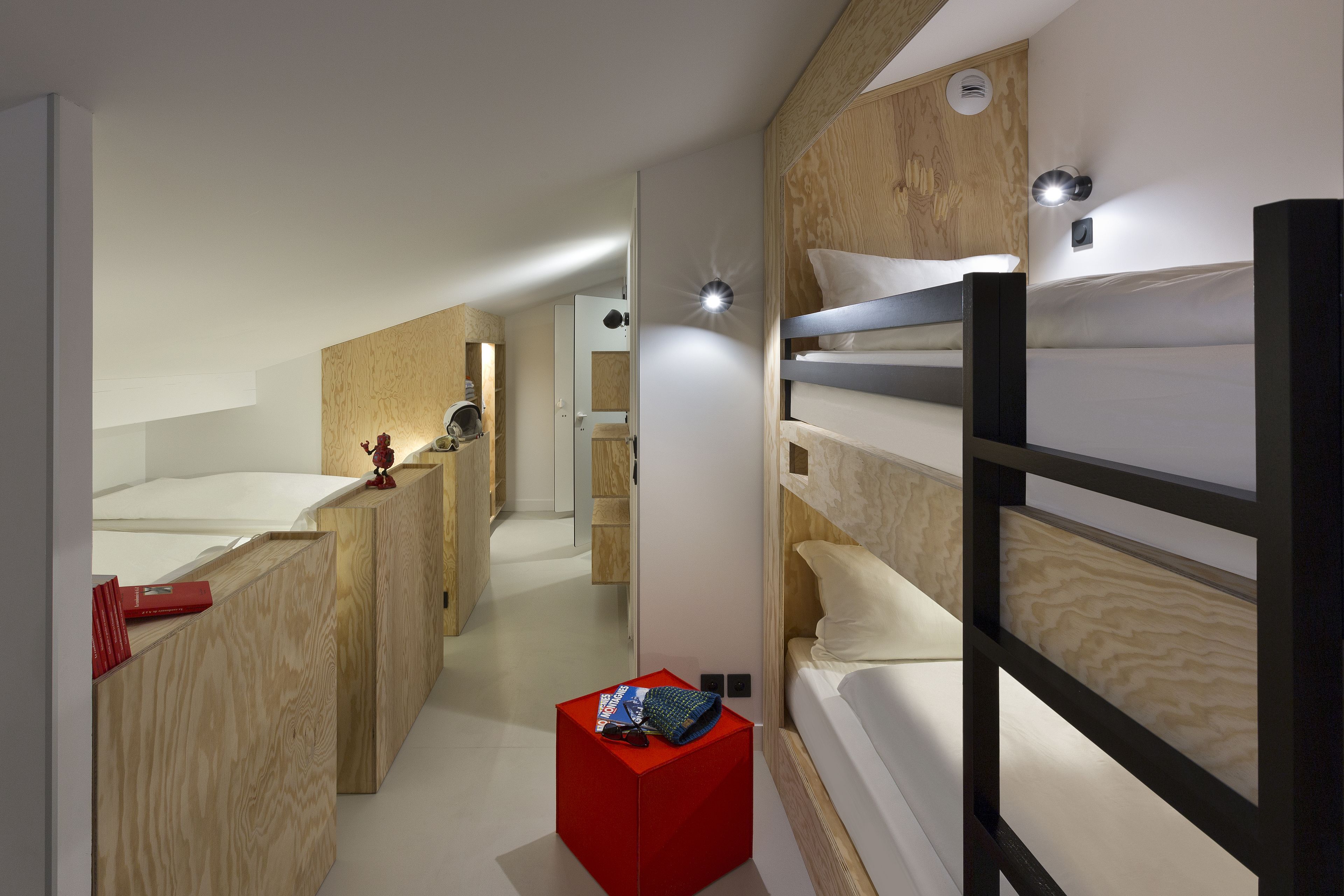 A modern hotel room with bunk beds, a wooden accent wall, and a small red box on the floor.