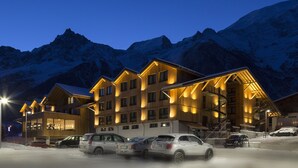 Un hotel de varios pisos con fachada de madera, múltiples balcones y un telesilla visible al fondo.