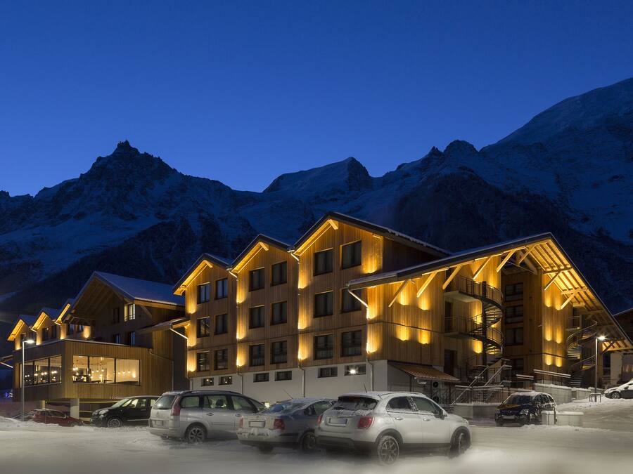 A multi-story hotel with a wooden facade, multiple balconies, and a ski lift visible in the background.