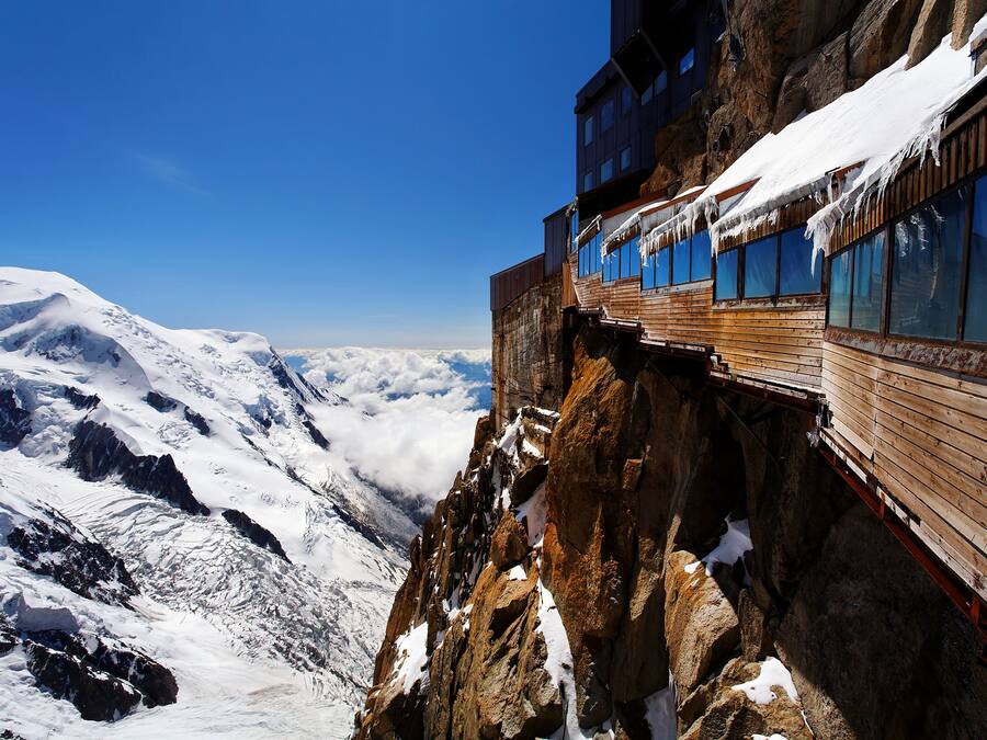 Un edificio de madera a gran altura, con amplios ventanales que dan a un paisaje nevado de montañas.