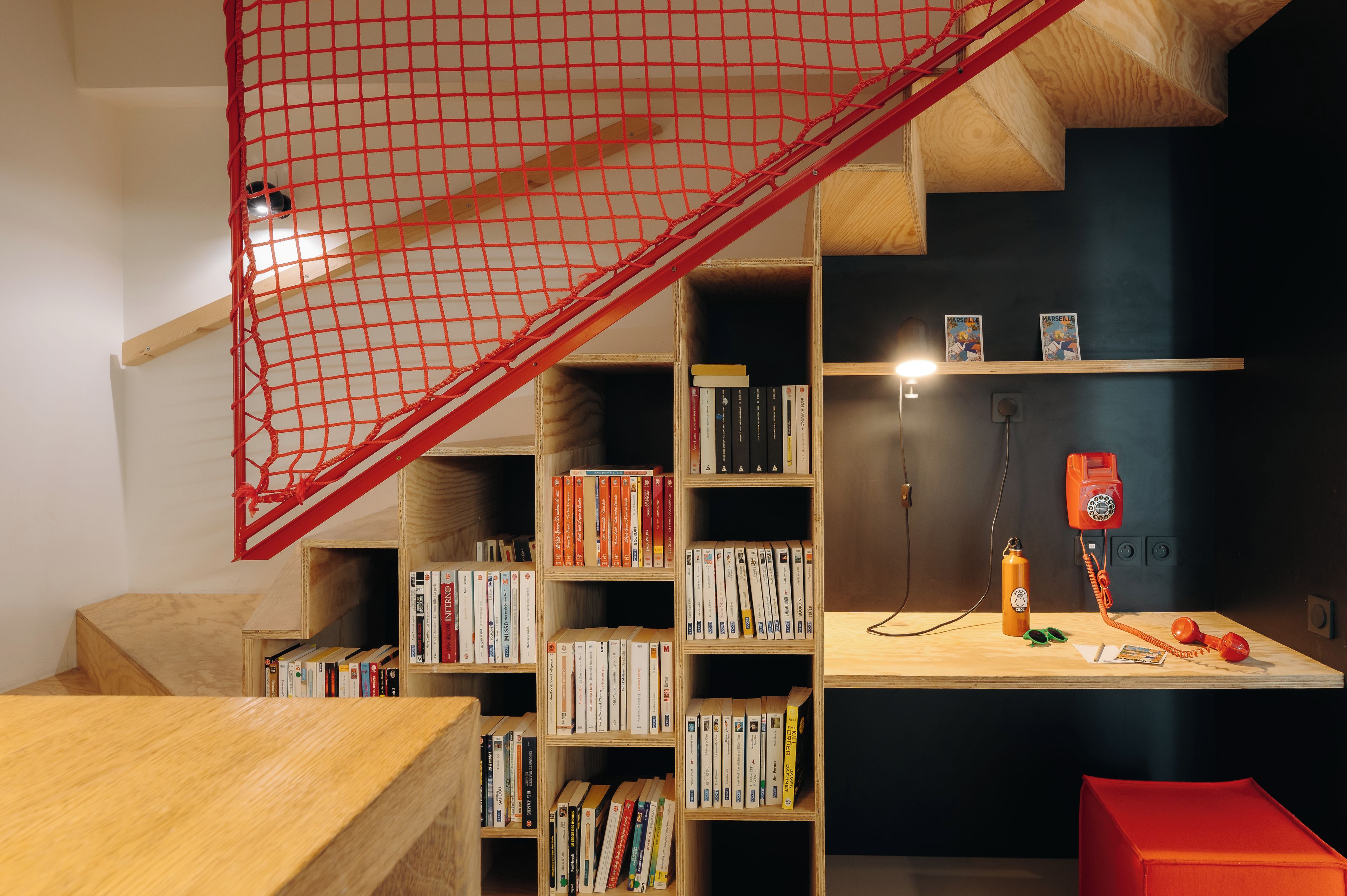Une pièce avec un escalier en bois, des étagères à livres, un bureau avec un téléphone et un filet rouge.