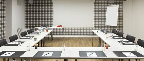A conference room with a long table, chairs, a whiteboard, and a projector screen.