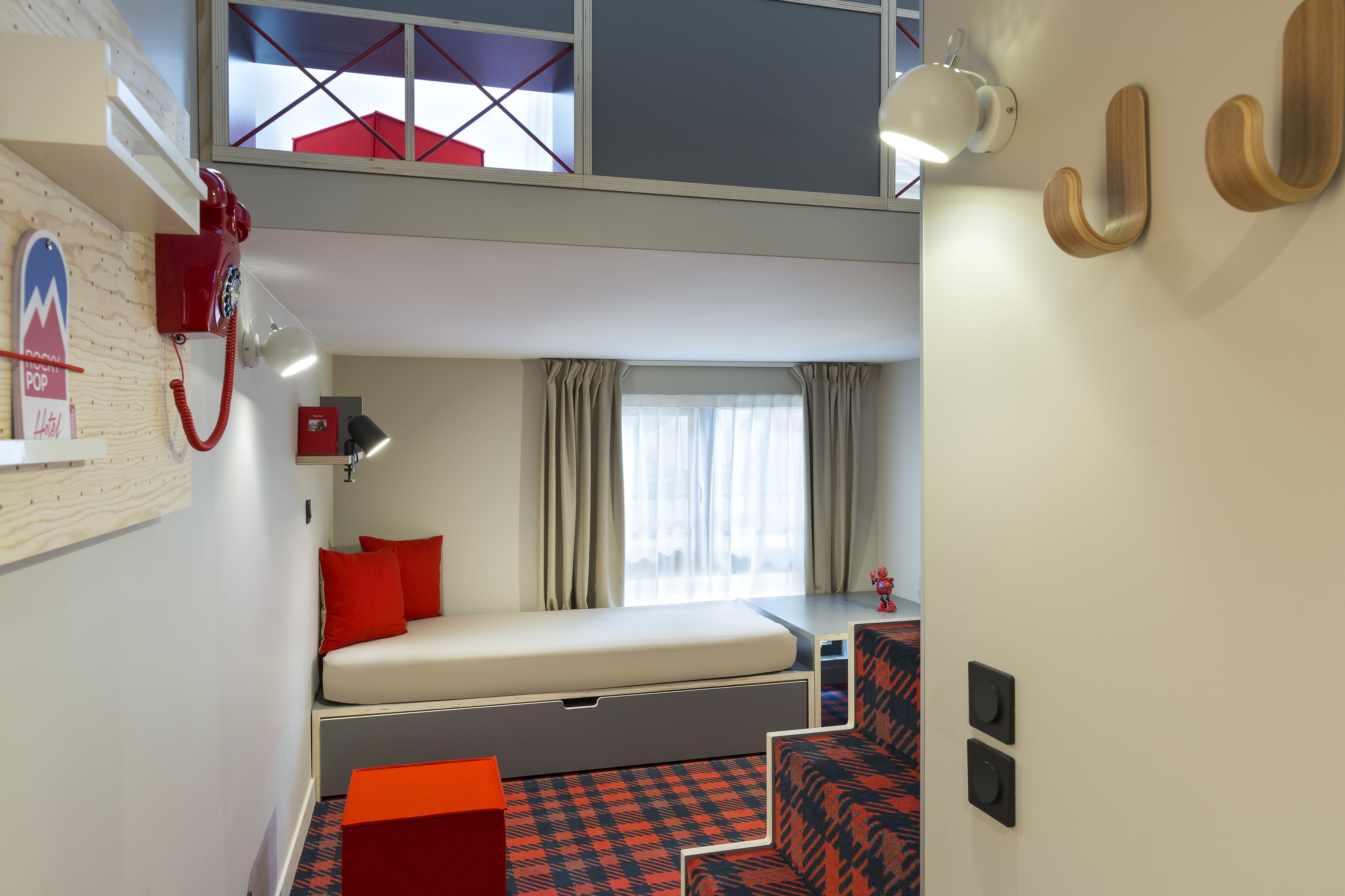 A compact hotel room with a bunk bed, a desk with a chair, a small table, and a red telephone.