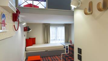 A compact hotel room with a bunk bed, a desk with a chair, a small table, and a red telephone.