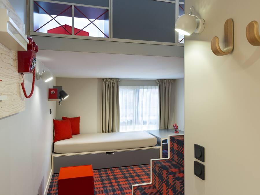 A compact hotel room with a bunk bed, a desk with a chair, a small table, and a red telephone.