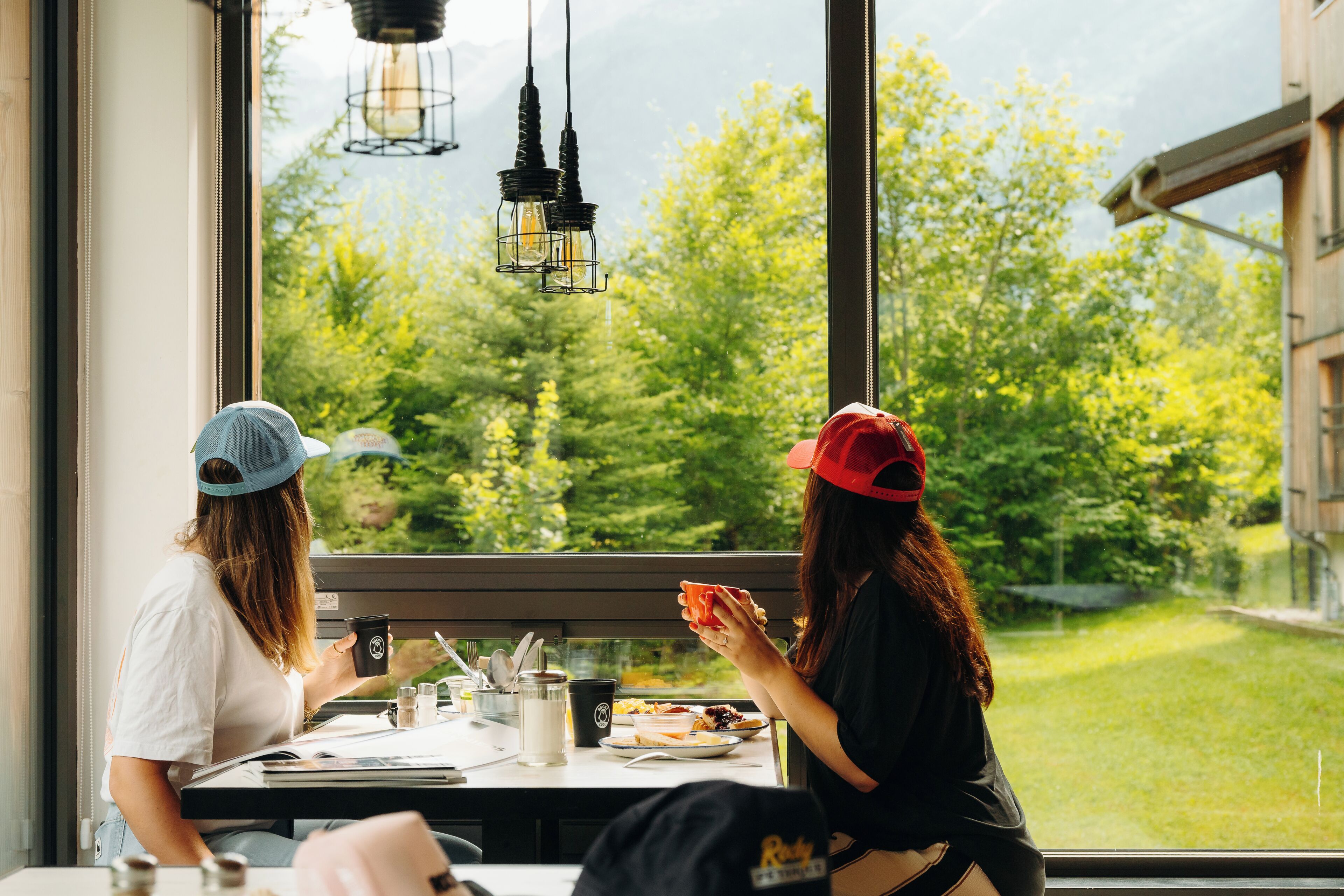 Two people seated at a table with a view of greenery outside a window.