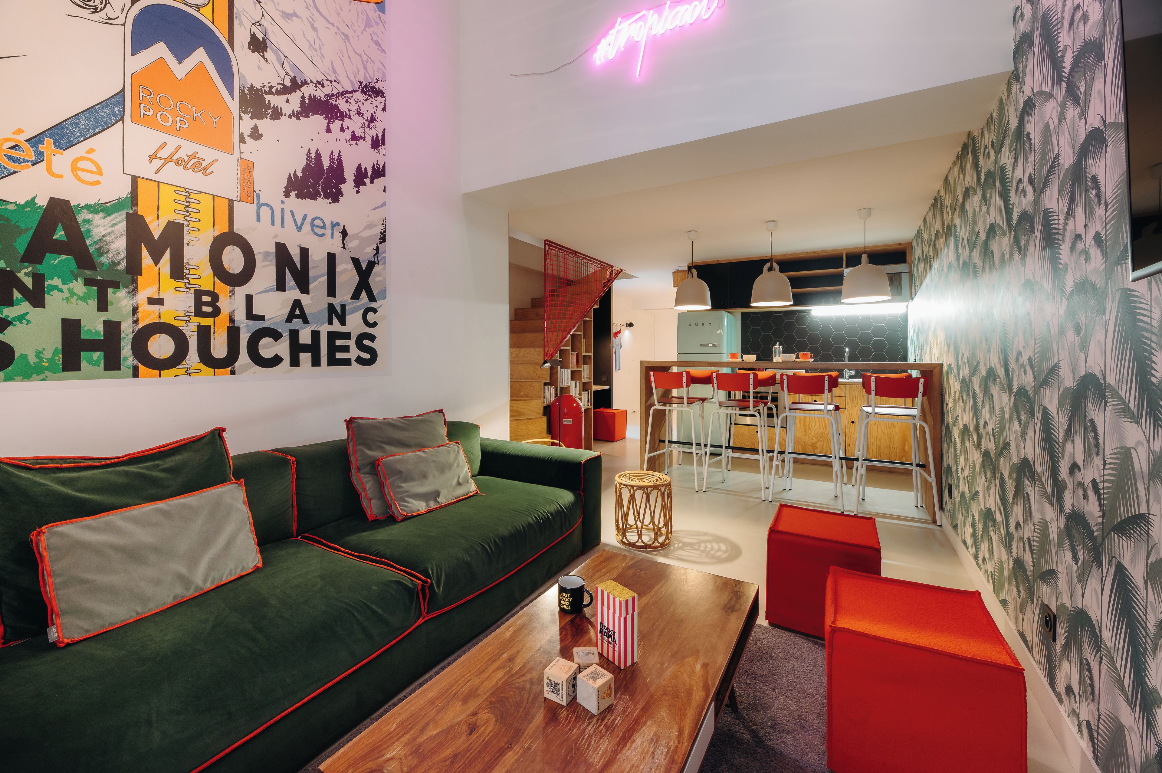 A modern living room with a green sofa, red accents, a wooden coffee table, and a kitchen area with bar stools.