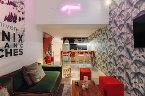 A modern living room with a green sofa, red ottoman, and a kitchen area with bar stools. - RockyPop Chamonix - Les Houches (Les Houches)