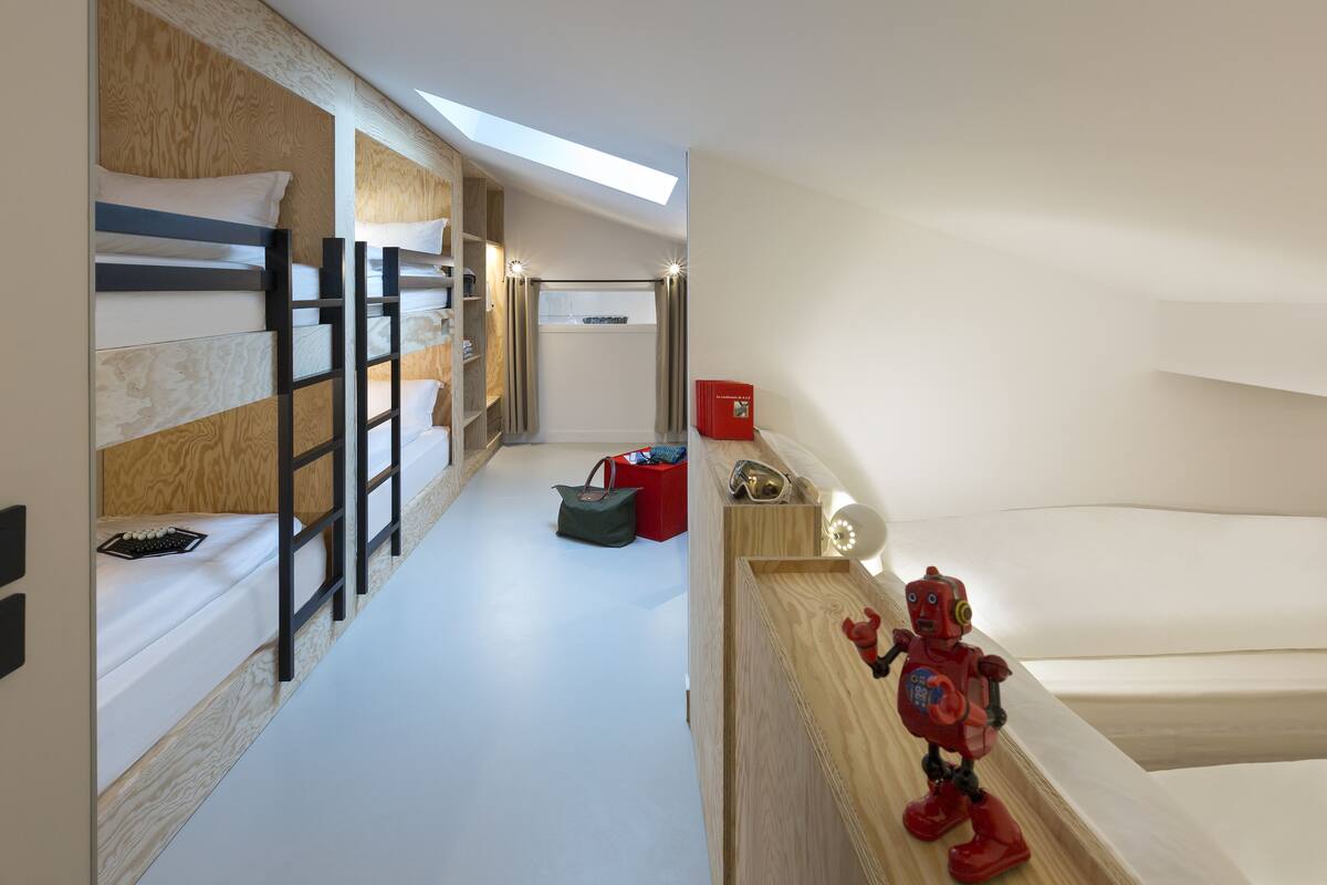 Une chambre d’hôtel moderne avec des lits superposés, une lucarne, une décoration à thème robotique rouge et une petite boîte rouge.