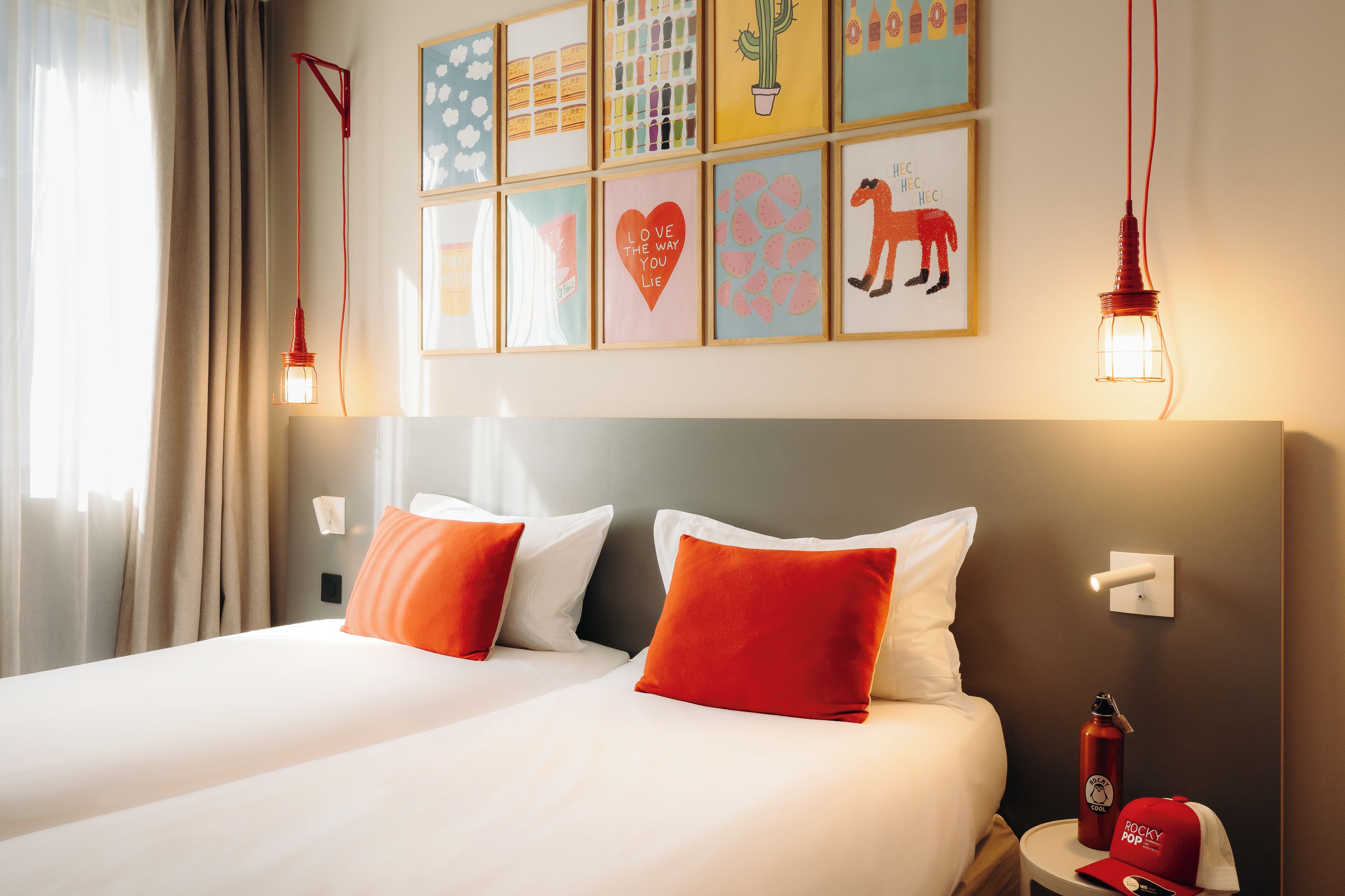 A hotel room with a bed, two pillows, a nightstand, a red water bottle, and wall art.