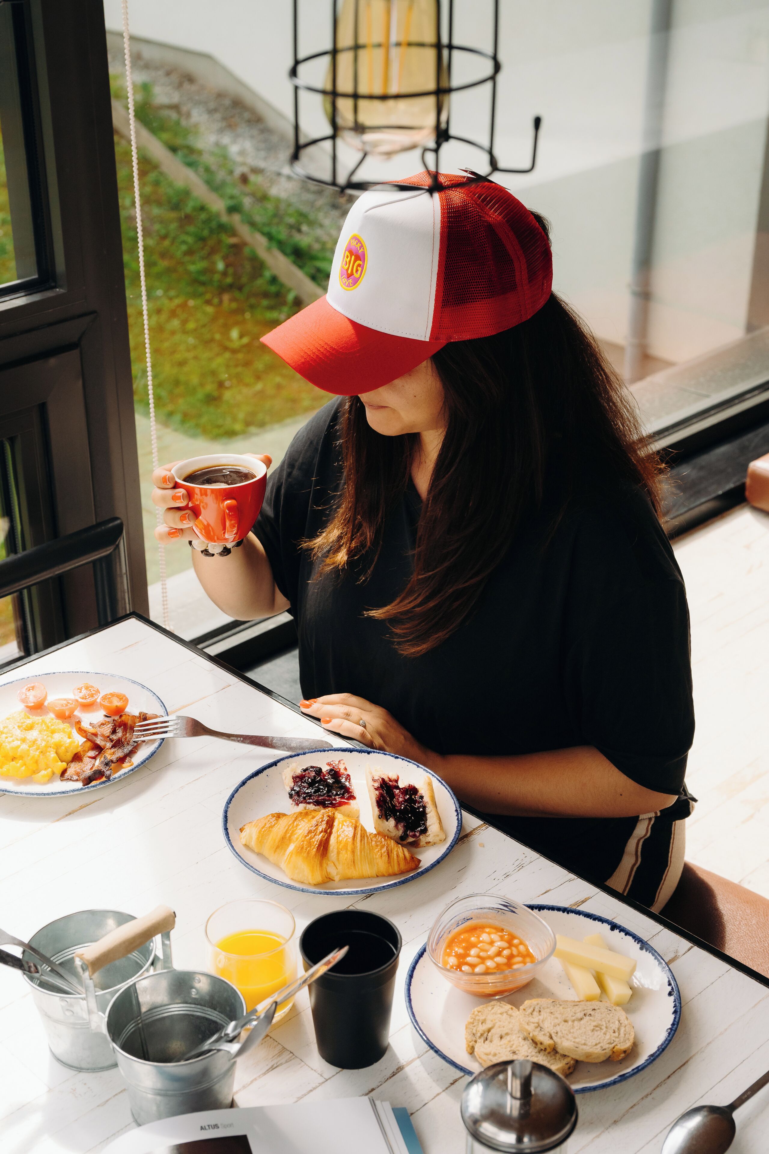 Una persona sentada a una mesa con alimentos para el desayuno, como croissants, frijoles y pan, además de una taza de café.