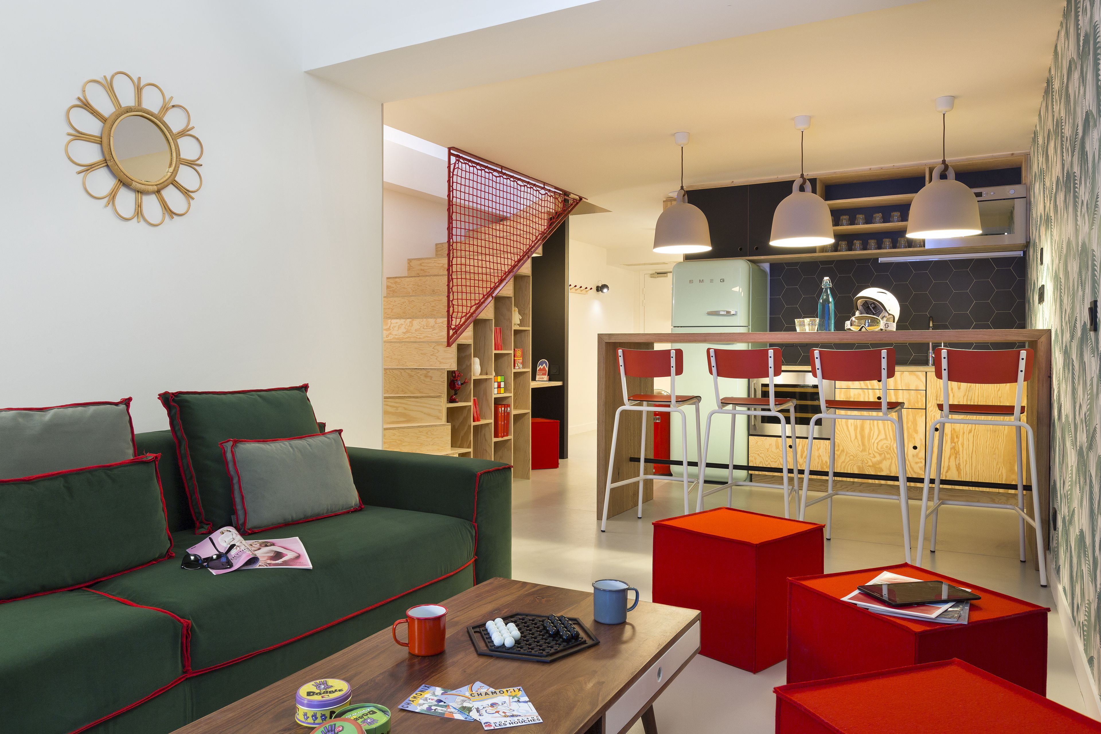 Un salon moderne avec un canapé vert, des touches de rouge, une table basse en bois et un coin cuisine doté d’un bar et de chaises rouges.