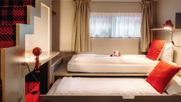A hotel room with two beds, a desk, a chair, a window with curtains, and a wall-mounted lamp.
