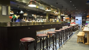 Una zona de bar con taburetes, una barra con botellas y lámparas colgantes.