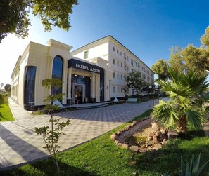 A hotel with a classic facade, a paved entrance, and a well-maintained garden. - Asson (Termez)
