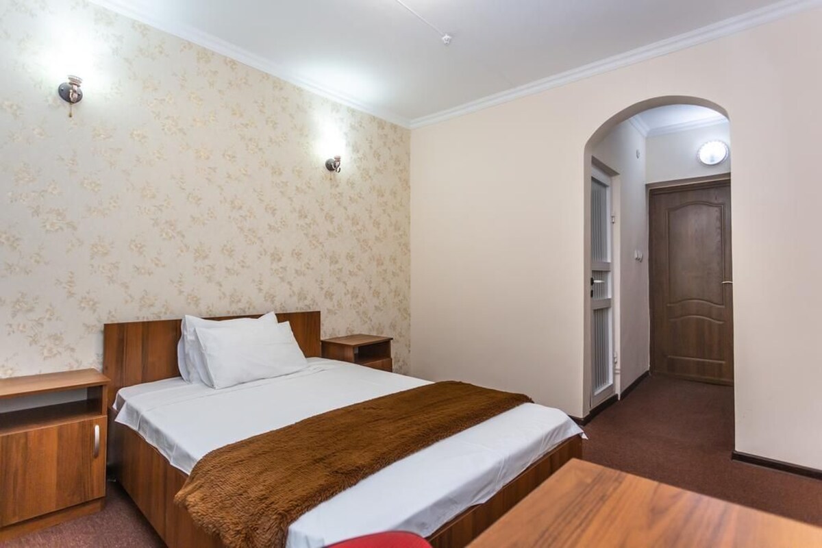 A bedroom with a bed, bedside tables, a wooden bench, a door, and a wall with a floral pattern.
