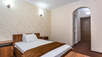 A bedroom with a bed, bedside tables, a wooden bench, a door, and a wall with a floral pattern.