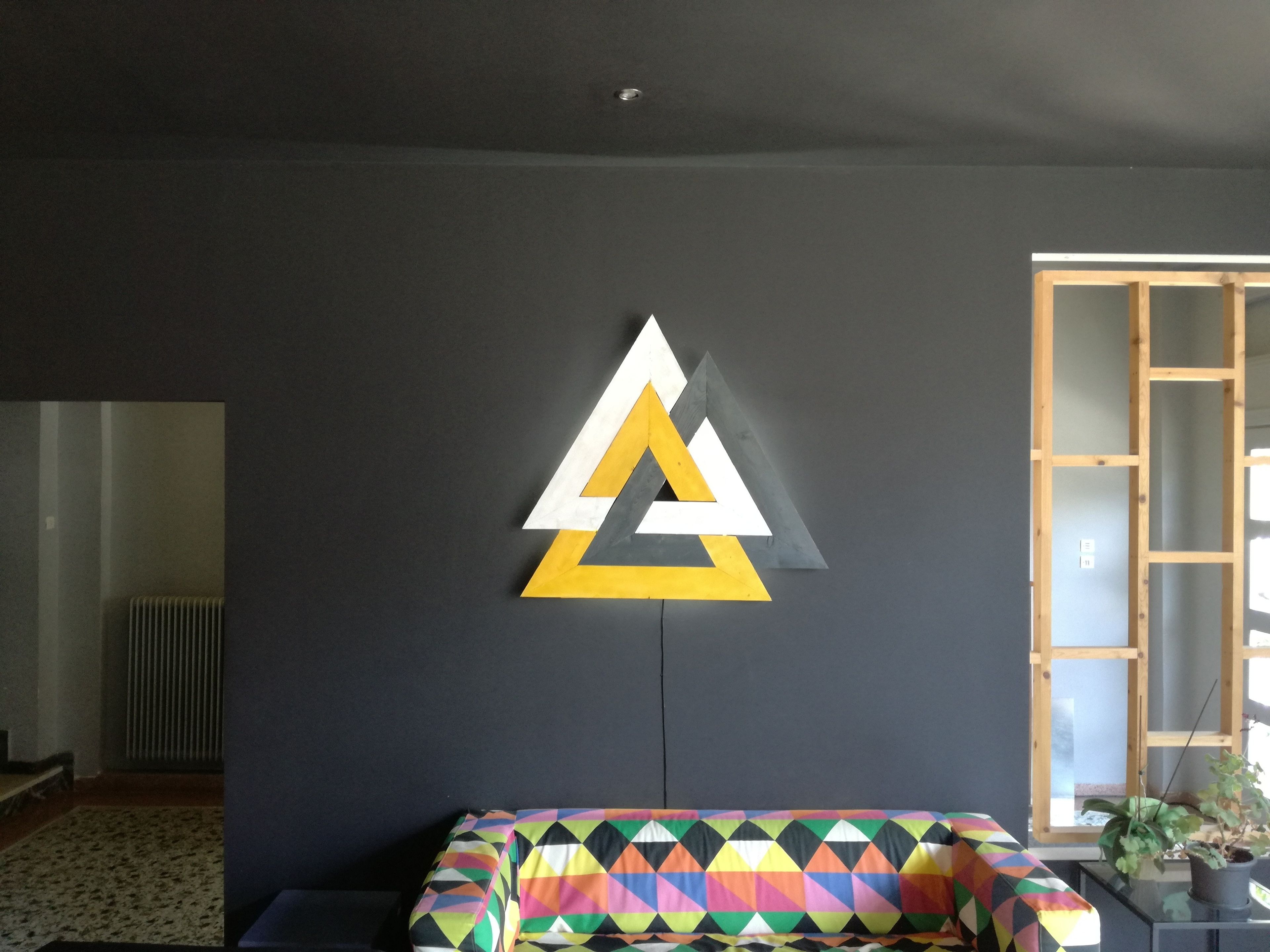 Ein Zimmer mit Wandkunst im geometrischen Stil, einem Bett mit farbenfroher Musterdecke und einem Fenster mit Blick ins Freie.