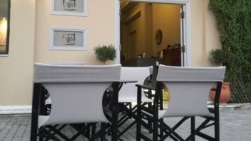 Une table et des chaises sont placées à l’extérieur d’un bâtiment sur lequel on peut lire l’inscription : « LEONIDION, maison d’hôtes ».