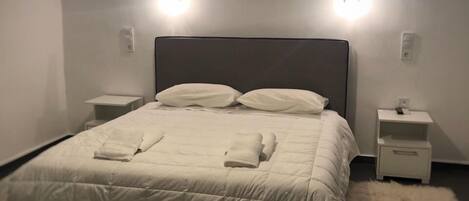 A neatly made bed with a white duvet and pillows, a fluffy rug, and two bedside tables with lamps.