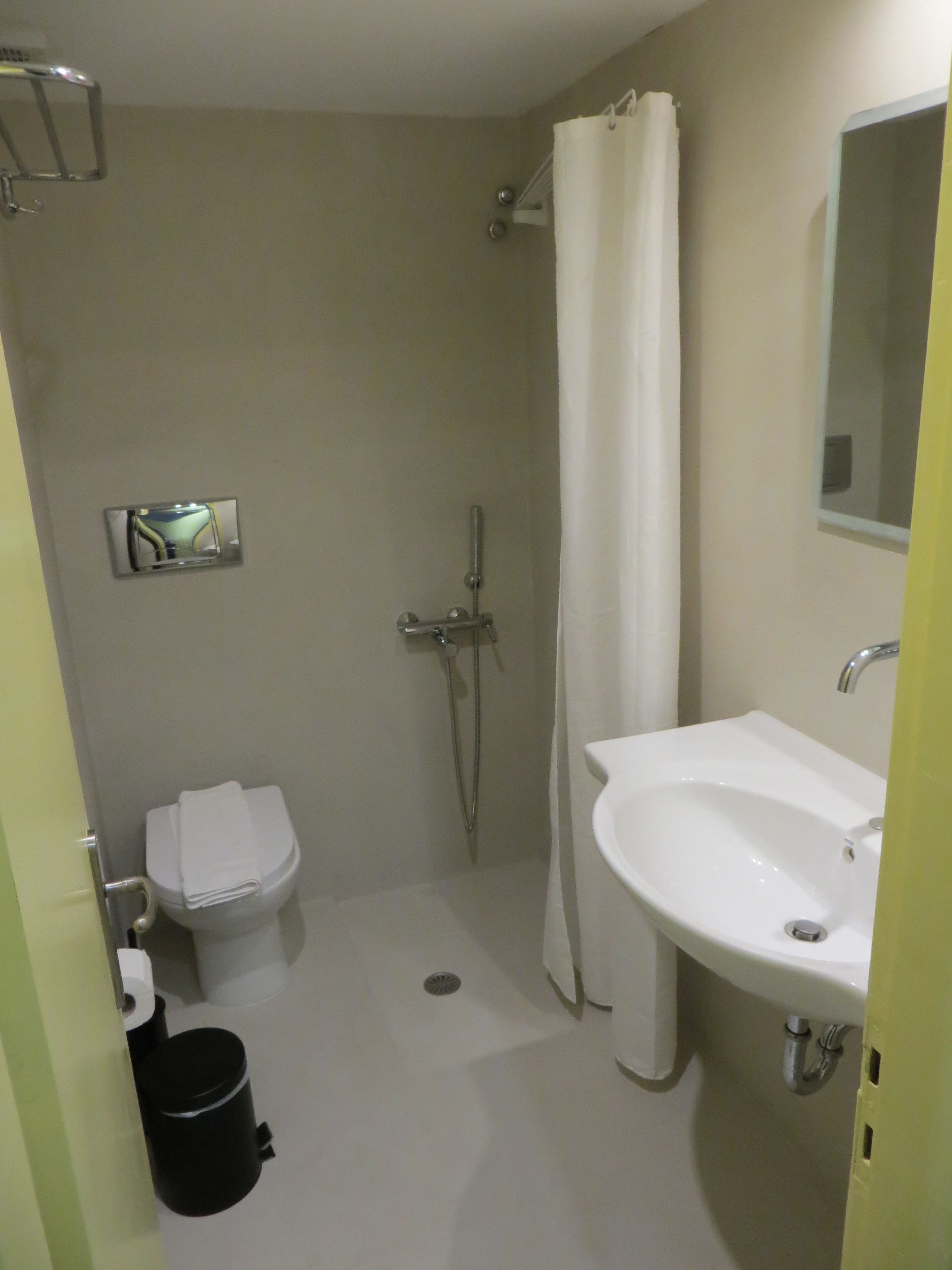 A bathroom with a toilet, sink, shower, and a mirror.