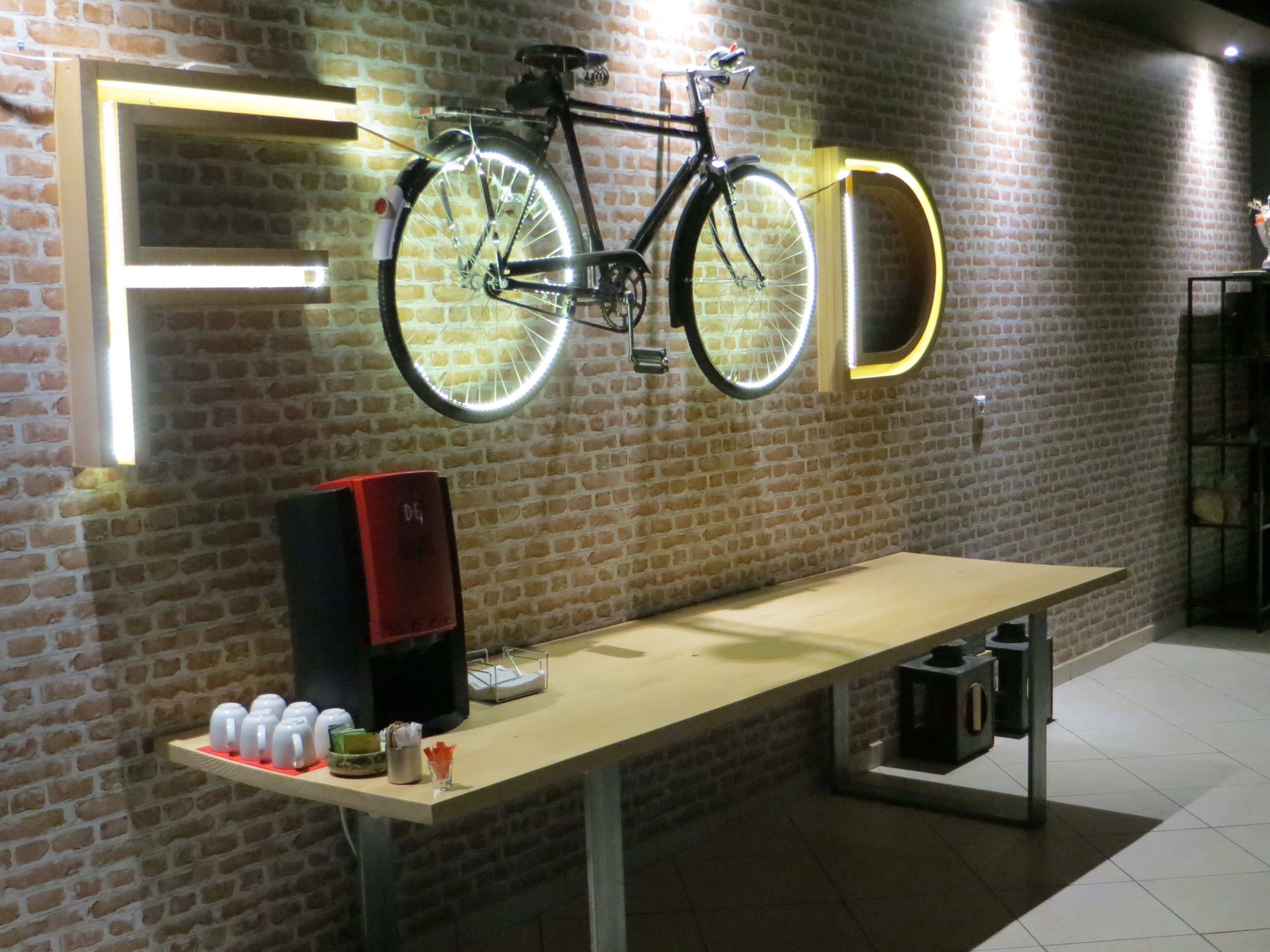 Un mur de briques avec un vélo suspendu au-dessus d’une table où sont exposés divers objets.