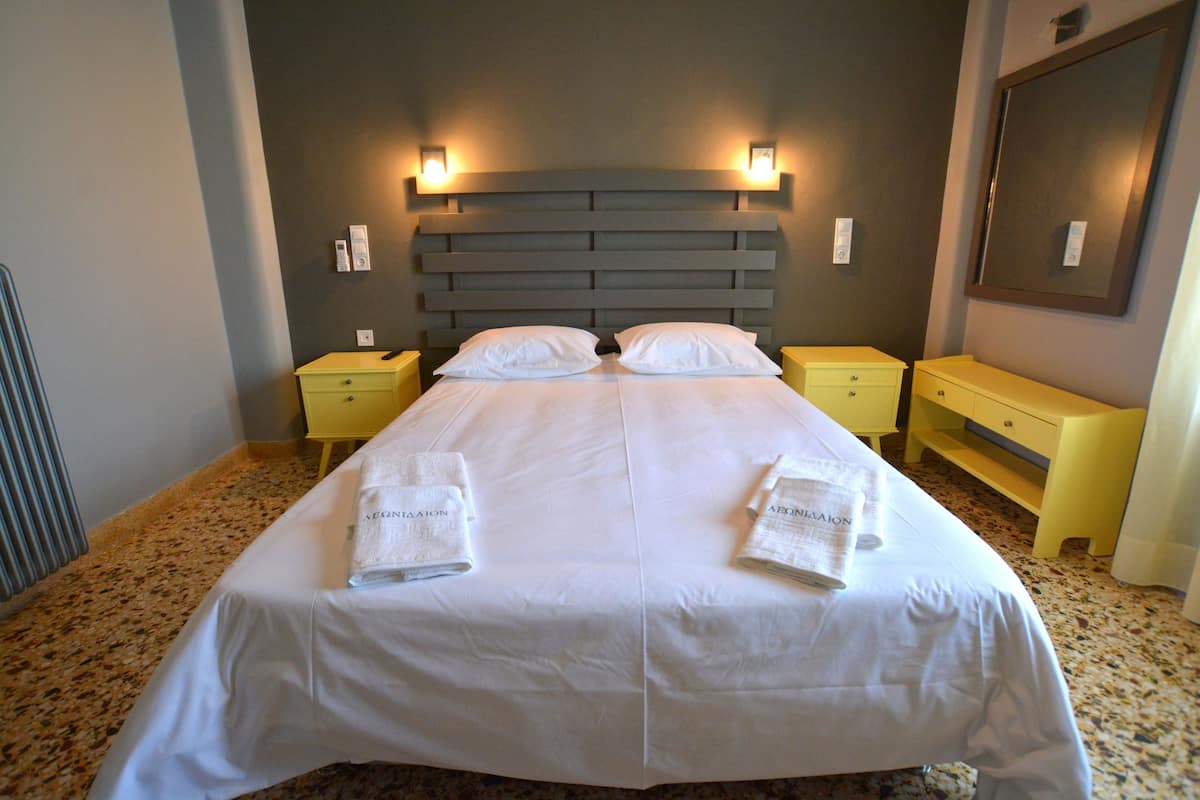 A double bed with white linens and two towels, a headboard with wall-mounted lights, and a mirror on the wall.