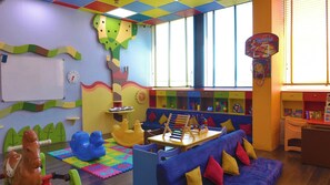 Uma área de recreação infantil colorida, com um sofá azul, uma mesinha e diversos brinquedos.