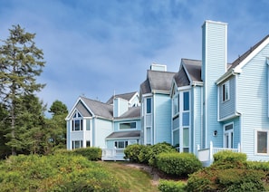 A large, light blue, multi-story house with a prominent chimney, surrounded by lush greenery and trees. - Worldmark Schooner Landing (Newport)