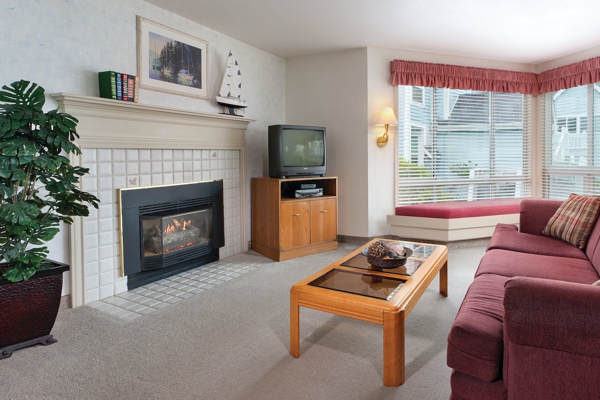A living room with a fireplace, a television, a sofa, and a window with blinds.