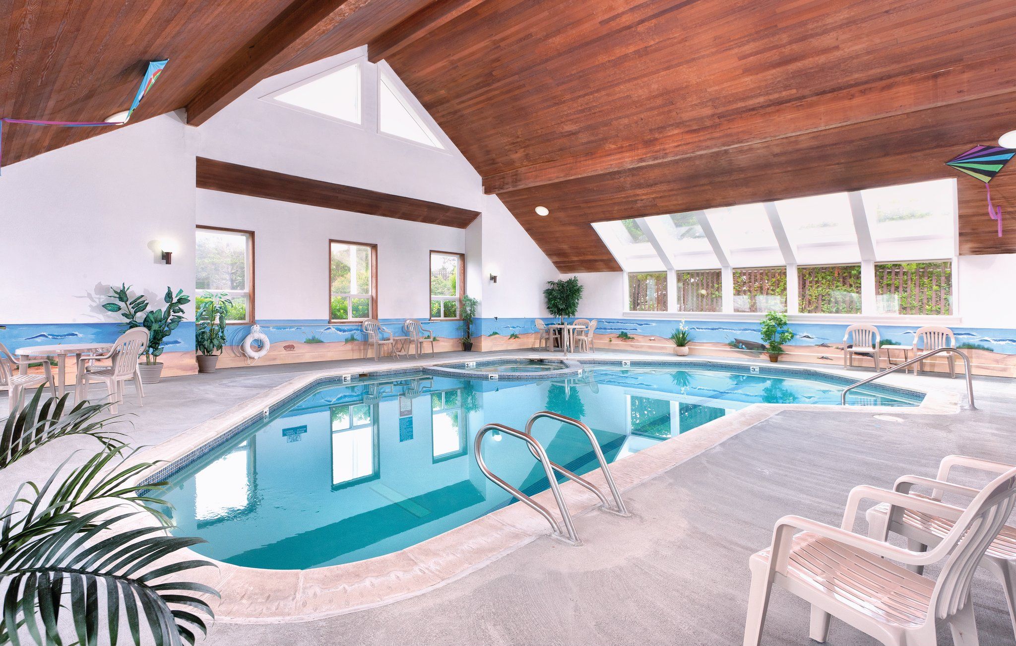 An indoor swimming pool with clear water, surrounded by lounge chairs and potted plants.