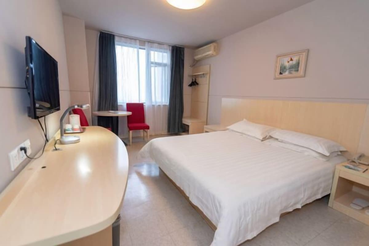 A hotel room with a bed, a desk with a chair, a television, and a small table.