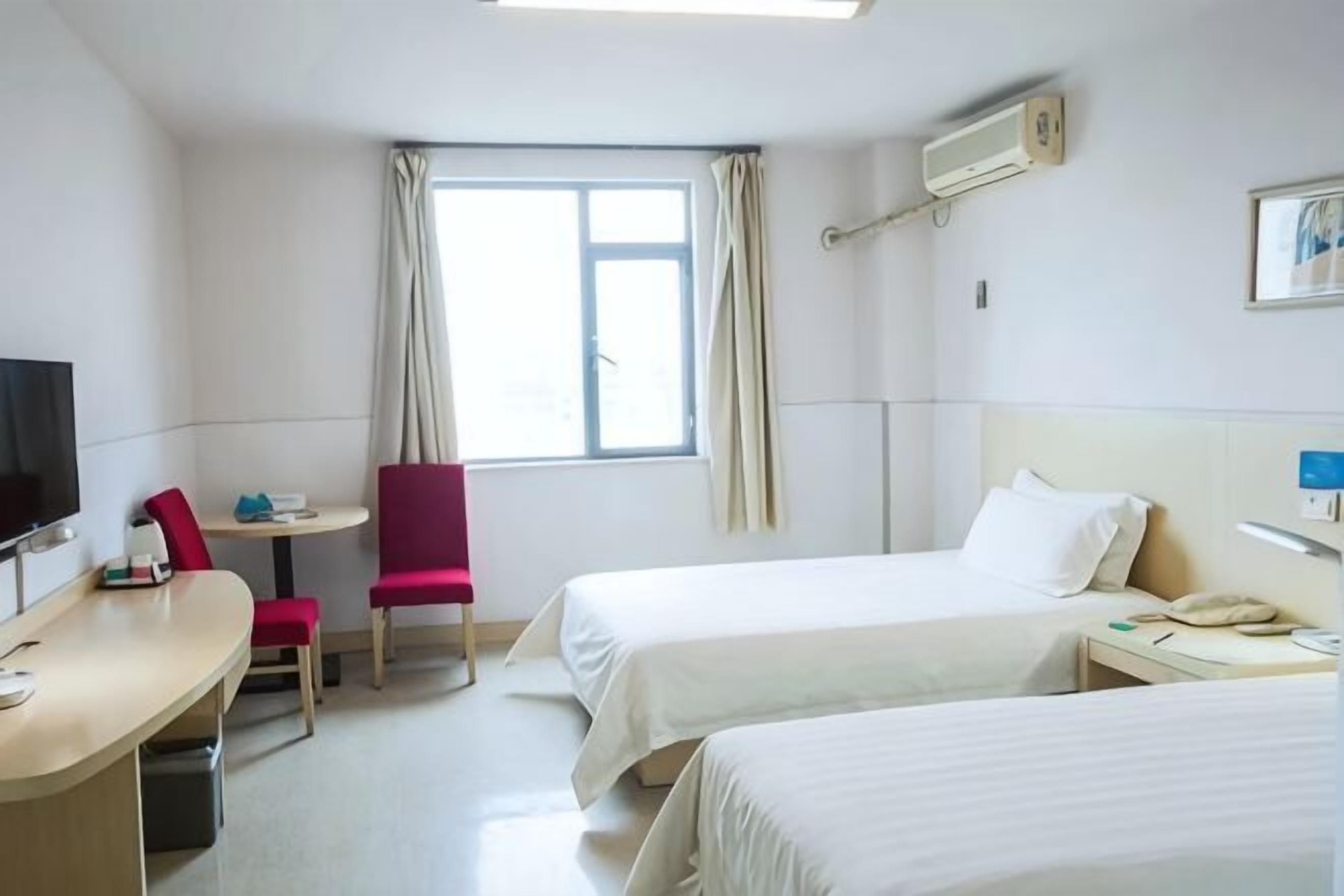 A hotel room with two beds, a desk, a chair, a TV, and a window with curtains.
