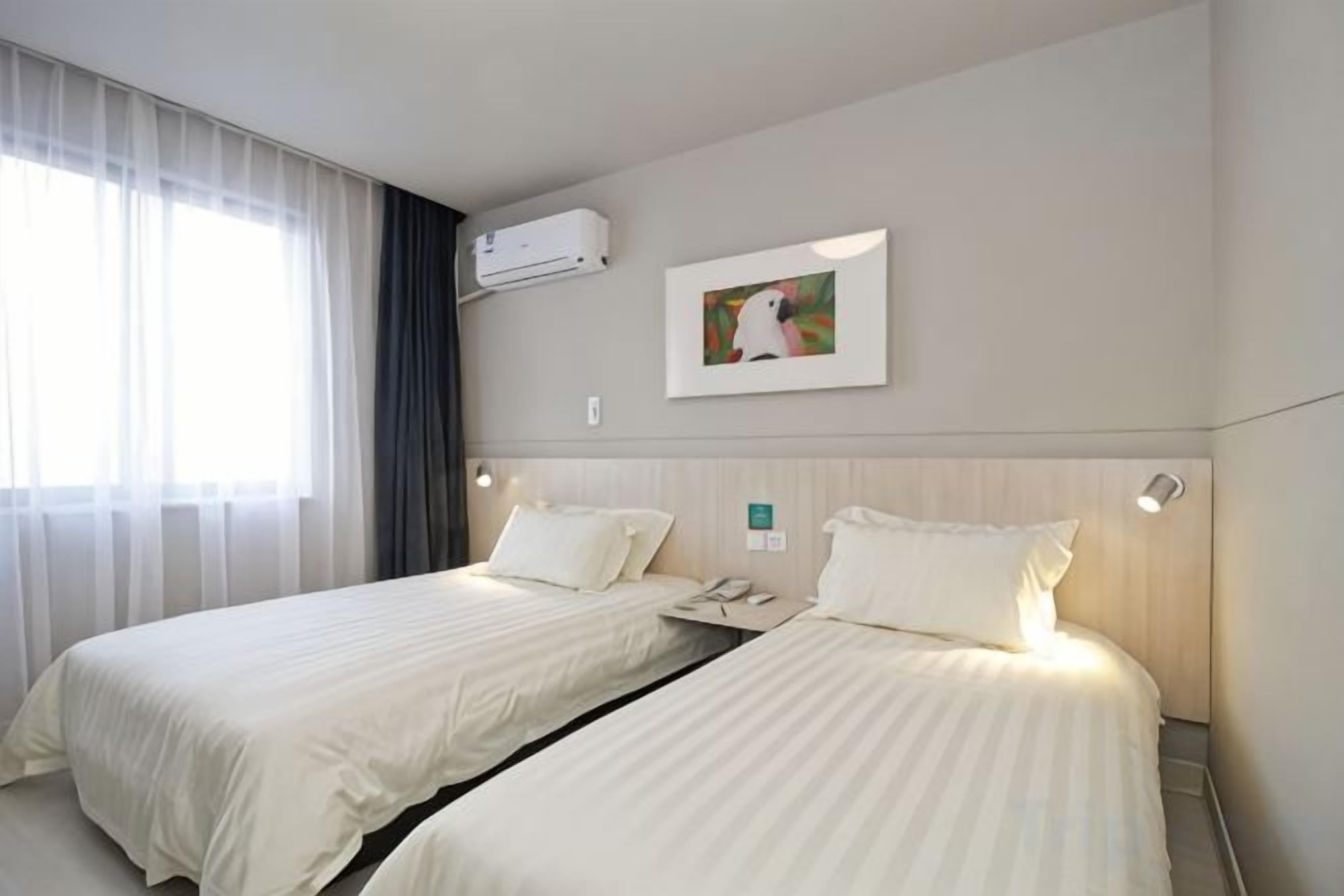 Habitación de hotel con dos camas, aire acondicionado de pared y un cuadro.