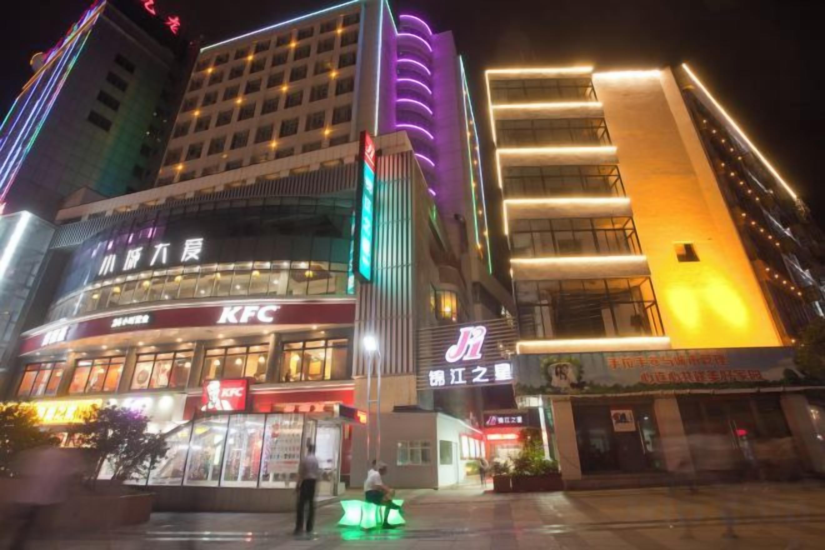 Un edificio de varios pisos con un restaurante KFC en la planta baja, un anuncio vertical grande e iluminación de entrada llamativa.