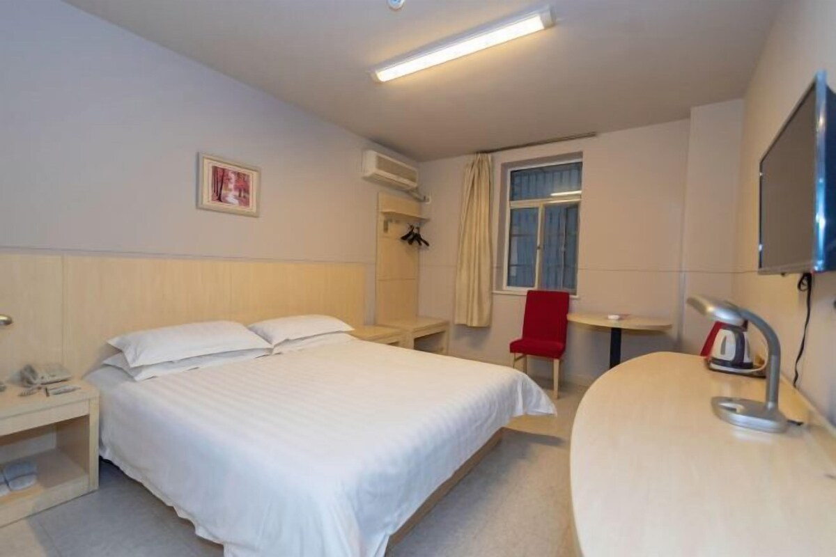 A hotel room with a bed, bedside table, chair, desk, and a TV.