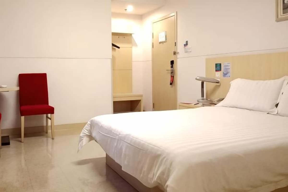 Ein Hotelzimmer mit einem Bett, einem roten Sessel, einem Schreibtisch und einem Spiegel.