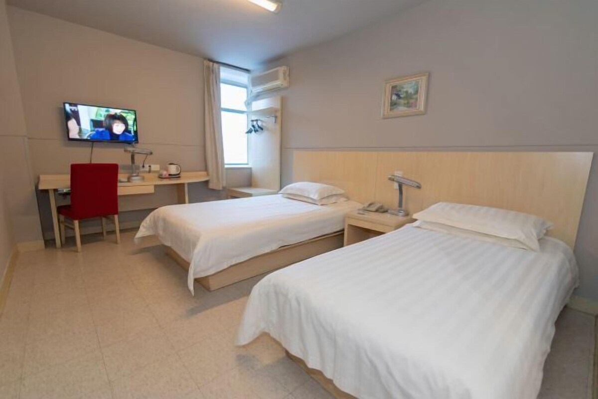 A hotel room with two beds, a desk with a chair, a TV, and a window with curtains.