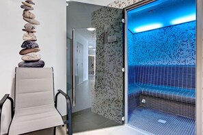 A spa area with a stone stack, a glass-enclosed hot tub, and a seating area with a chair. - Brit Hotel Vendee Mer (Les Achards)
