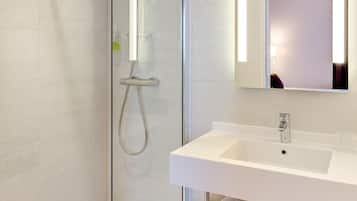 Un baño moderno con ducha envuelta en vidrio, un lavamanos blanco y un espejo.