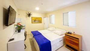 Ein Hotelzimmer mit Bett, Schreibtisch, Sessel, Fernseher, Pflanze und Fenster.