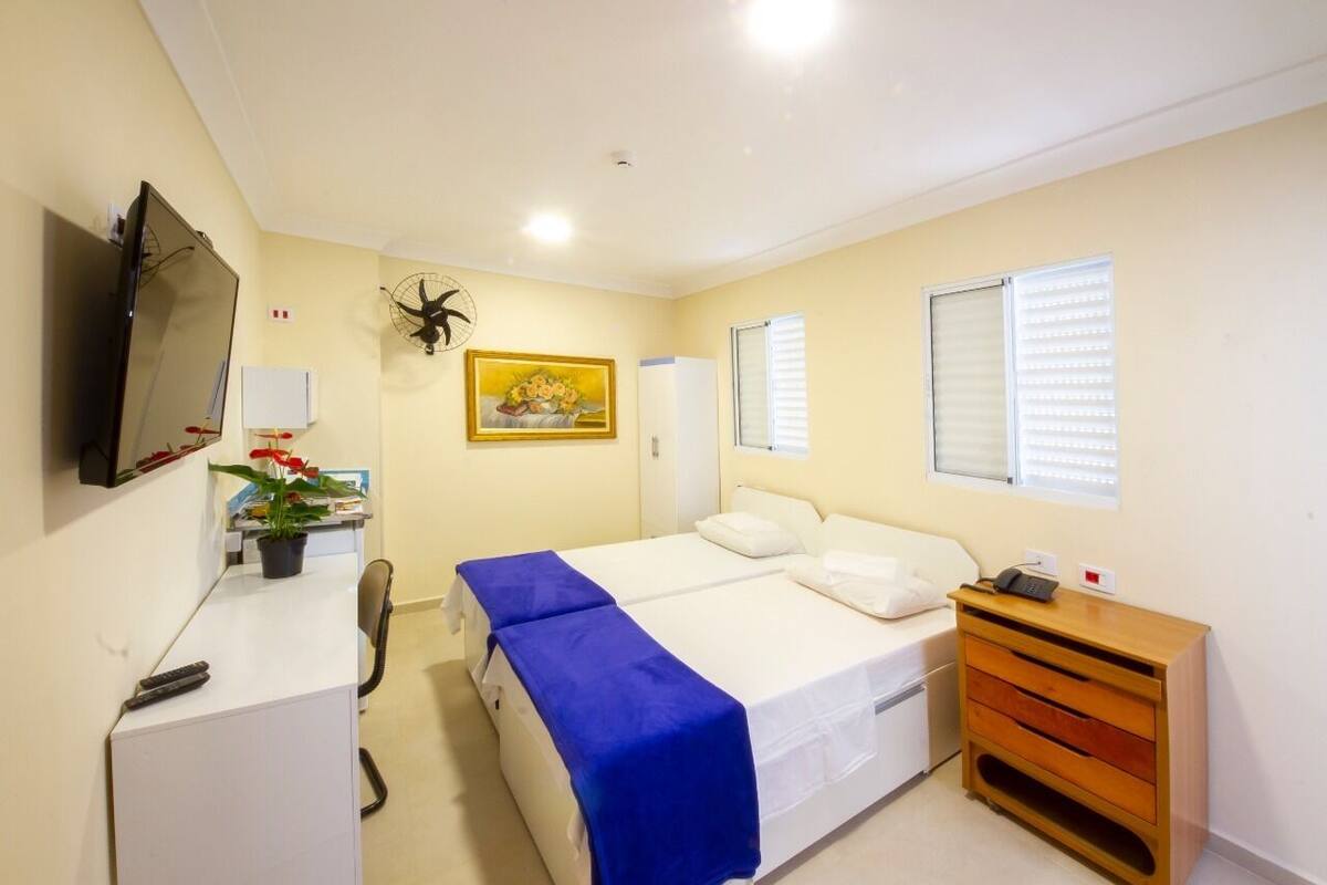Ein Hotelzimmer mit Bett, Schreibtisch, Sessel, Fernseher, Pflanze und Fenster.