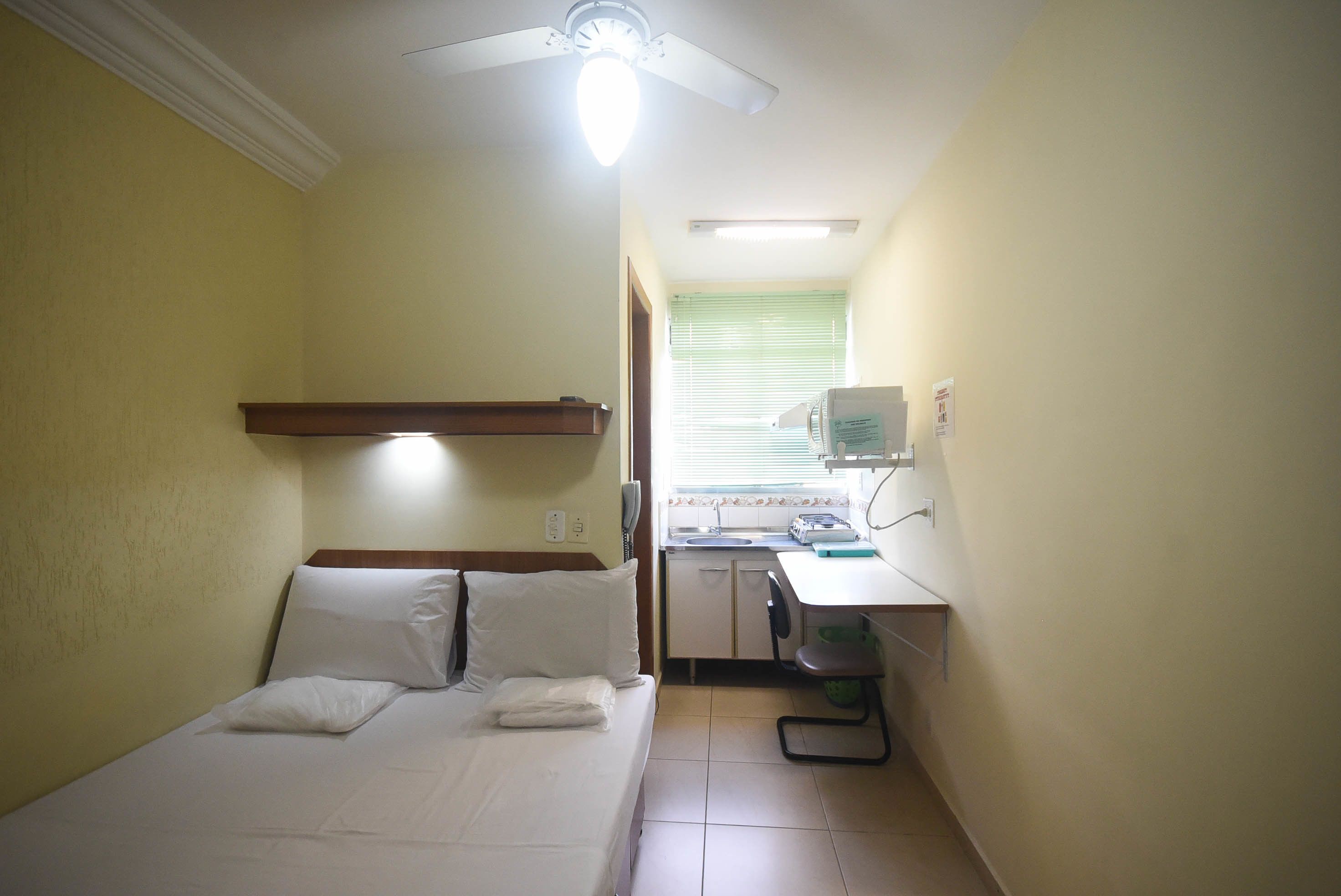 Una camera d'albergo piccola e funzionale con un letto singolo, una scrivania e angolo cottura.
