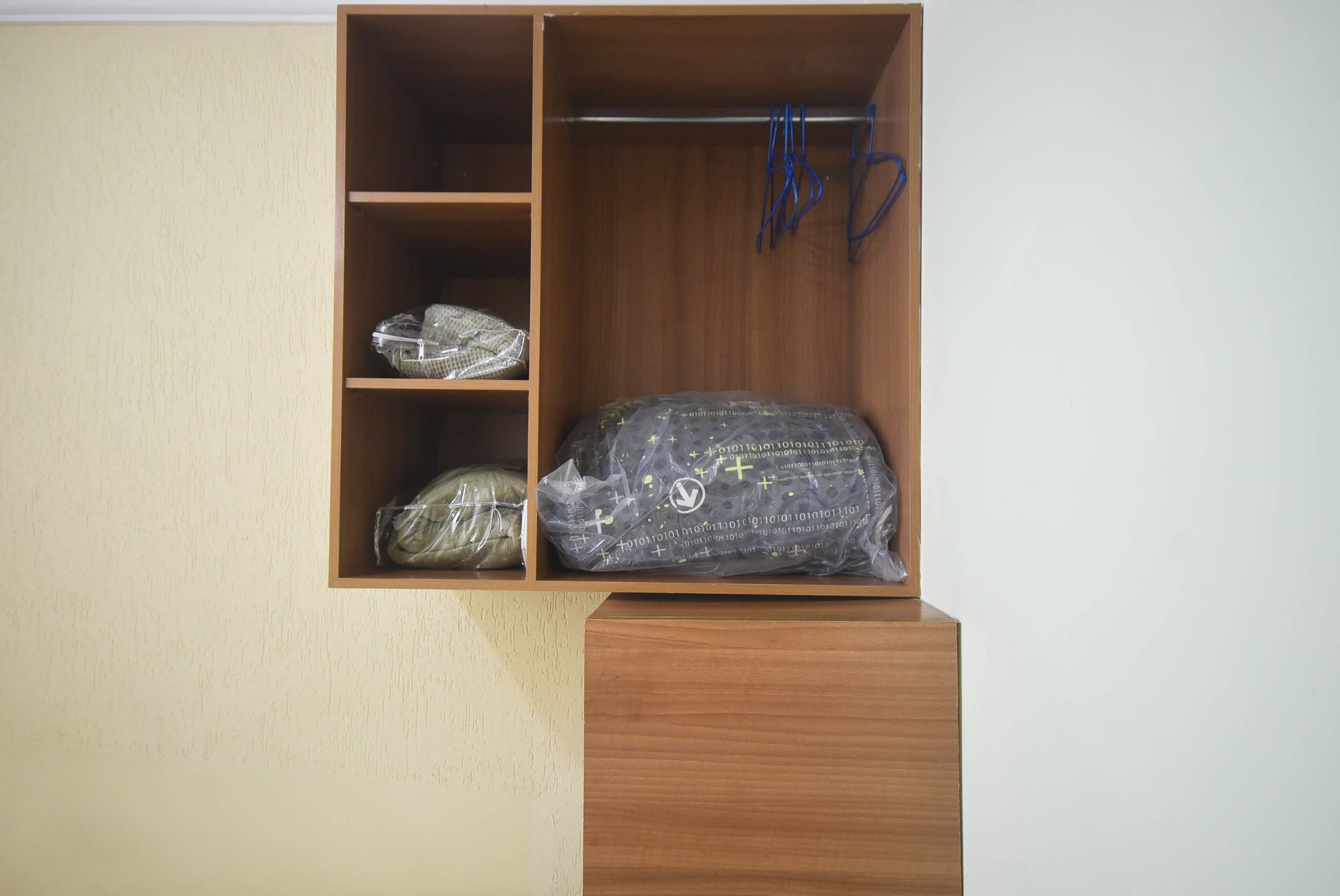 A wooden wardrobe with three shelves, one of which contains a wrapped item and another with a hanging blue cord.
