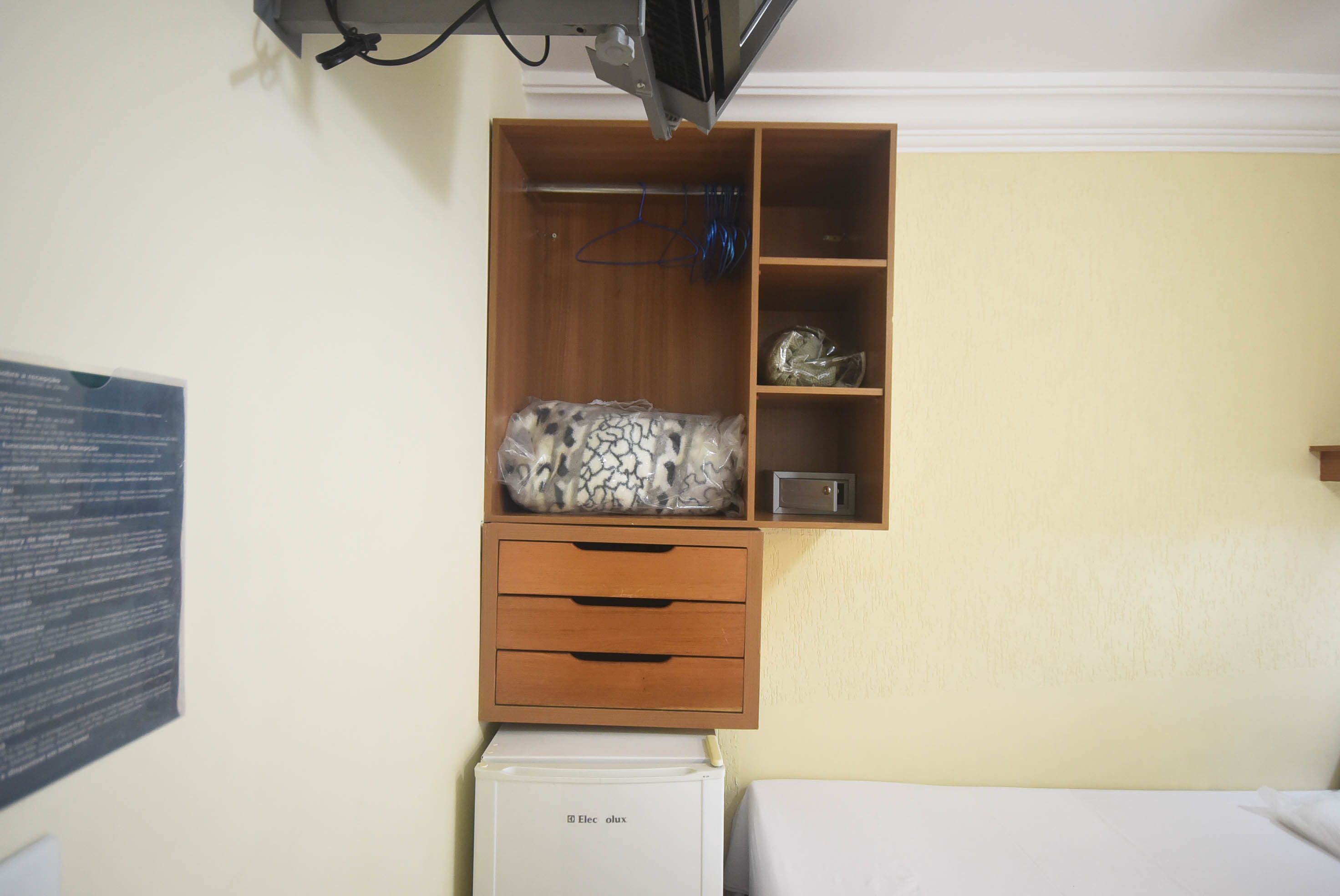 Une petite chambre comprenant une armoire en bois, un petit réfrigérateur et un lit.