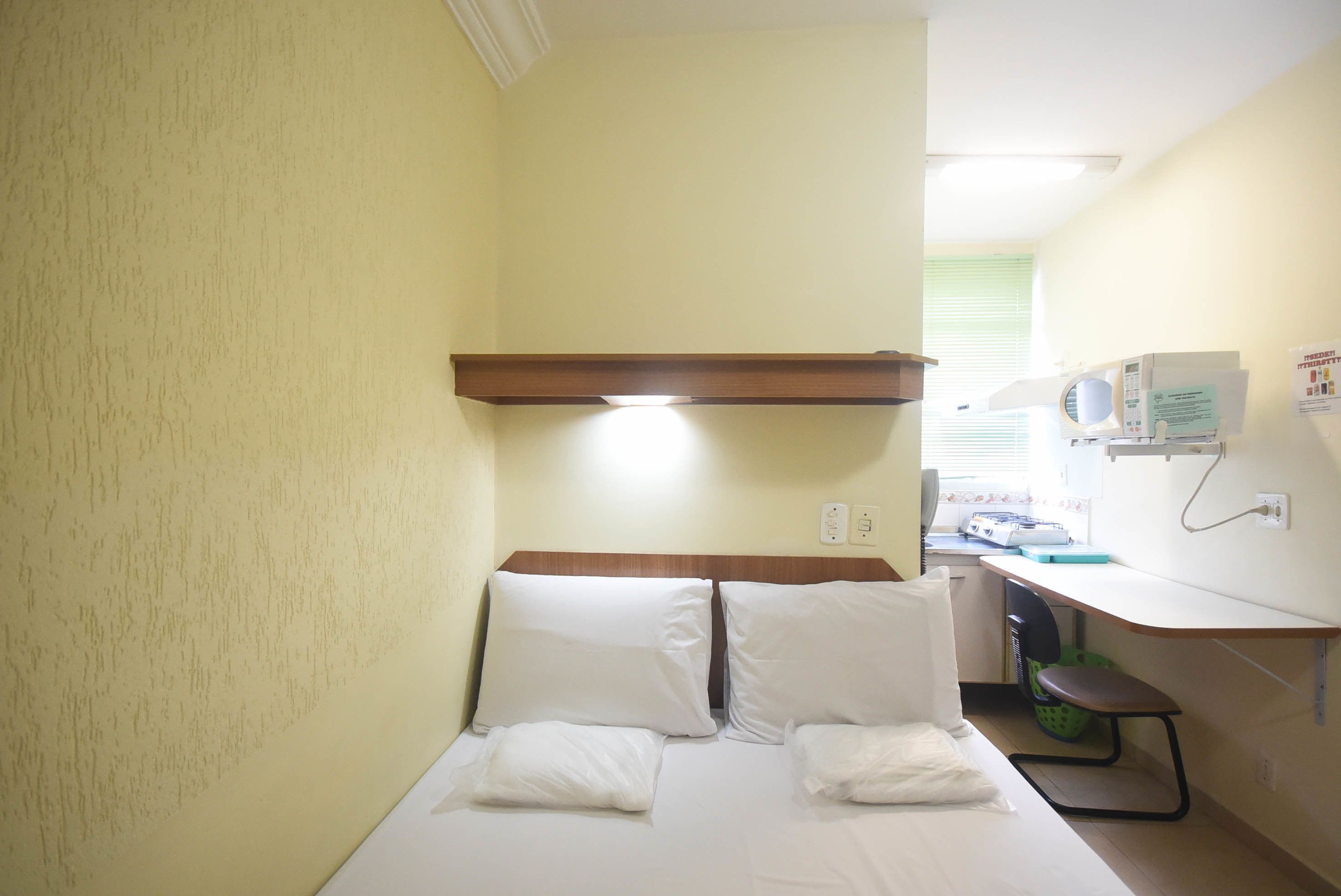 A small hotel room with a bed, a desk, and a microwave.