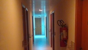 Ein schmaler, mit Fliesen ausgelegter Gang mit Türen an beiden Seiten, einem an der Wand befestigten Feuerlöscher und einer Deckenleuchte.